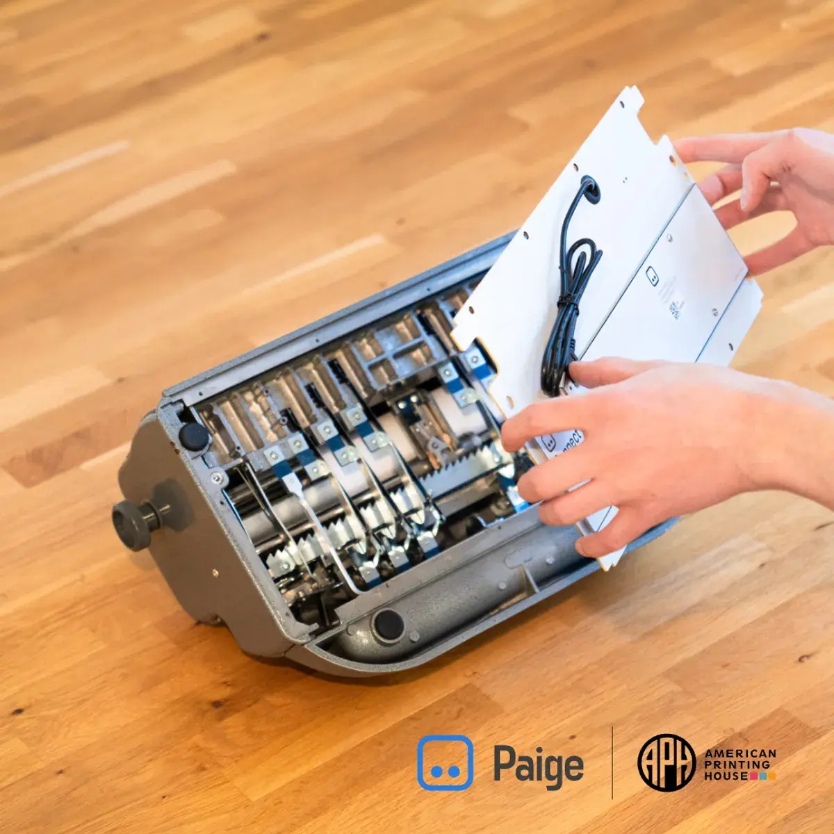 Hands installing the Paige Connect hardware inside a braille writer, with logos of Paige and the American Printing House visible at the bottom.